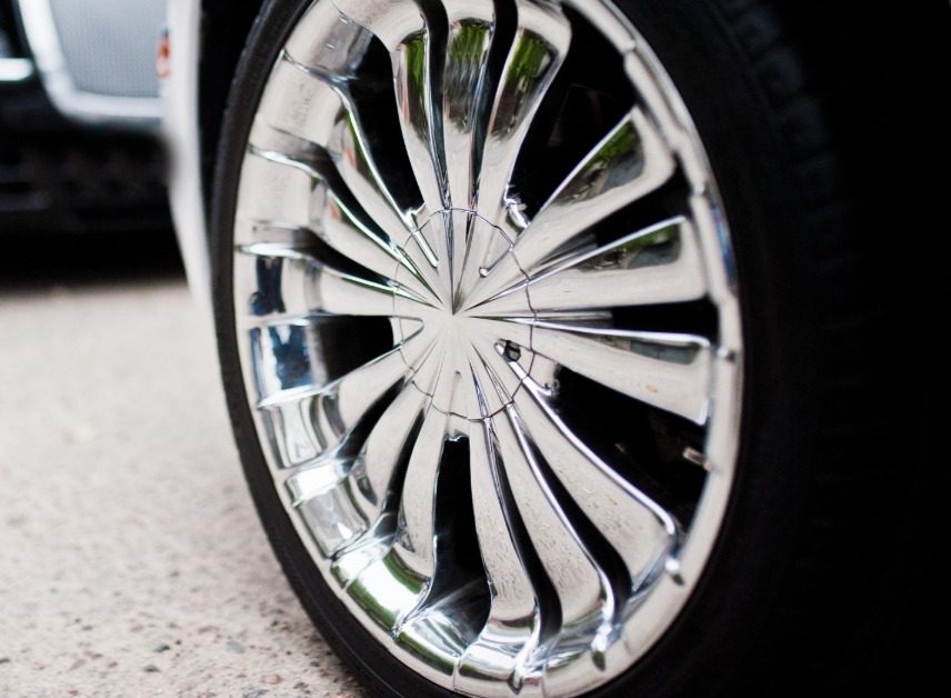 A close-up of a white car's shiny chrome wheel parked on a pavement with a black car opposite facing it.