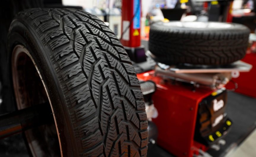 A close-up of a new tire. Another tire, blurred in the background, lies flat on a balancing machine.