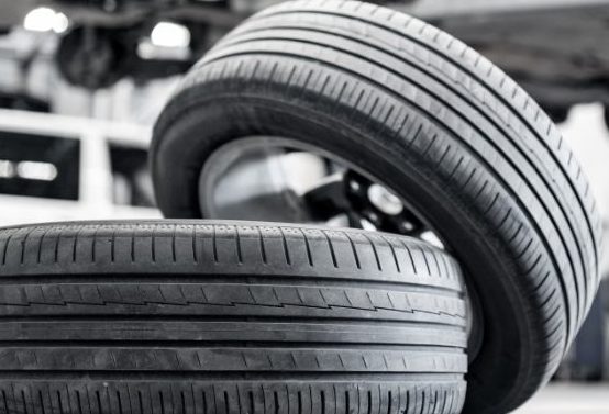 A couple of tires lie haphazardly on the ground of a shop floor. A red SUV is lifted with no tires on.