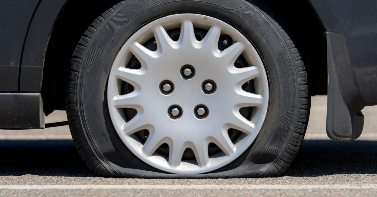 A close-up side view of a wheel with a flat tire attached to a black car resting on pavement with white lines.