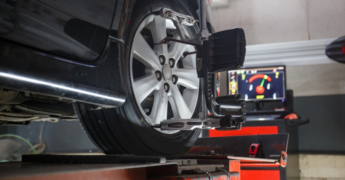 A close-up of a sensor attached to the wheel and tire of a vehicle. A computer shows data in the background.