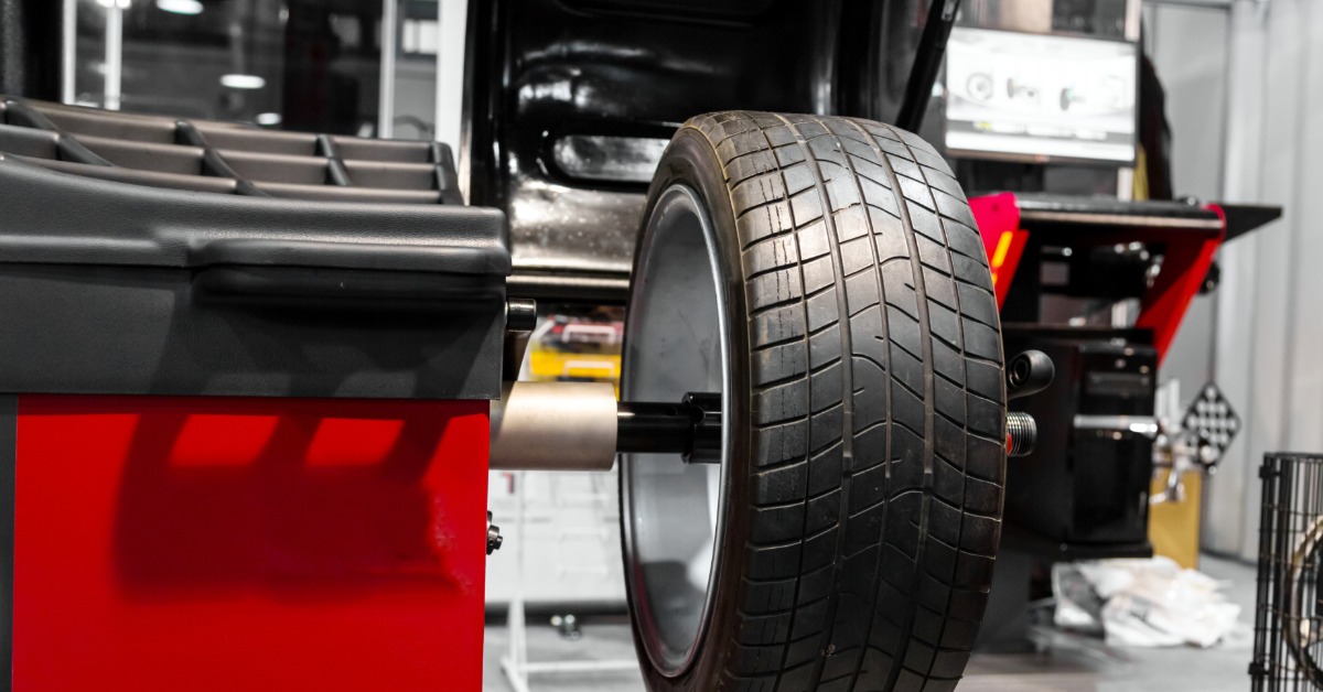 A tire is attached to a machine for rebalancing. Other automotive parts and equipment are in the background.