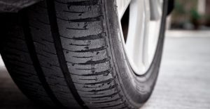 A close-up of a tire resting on a concrete surface. The tire is bald, with very worn tread on the outer edge.