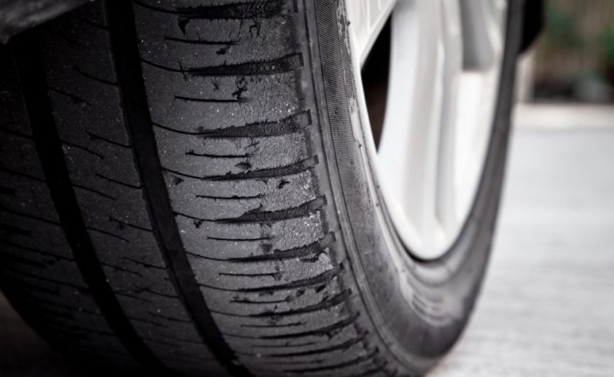 A close-up of a tire resting on a concrete surface. The tire is bald, with very worn tread on the outer edge.