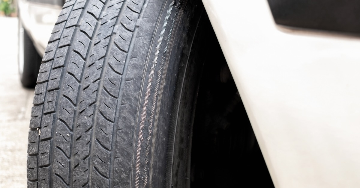 A close-up view of a badly worn tire with exposed metal wire cords visible across the tread surface.