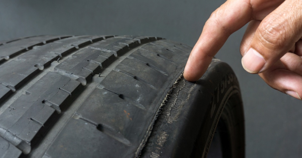 A person pointing at damaged tread on a black tire, with uneven wear visible along the rubber surface.