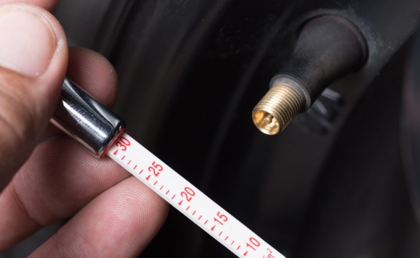 A close-up of a hand holding a tire pressure gauge next to the open brass tire valve stem of a tire.