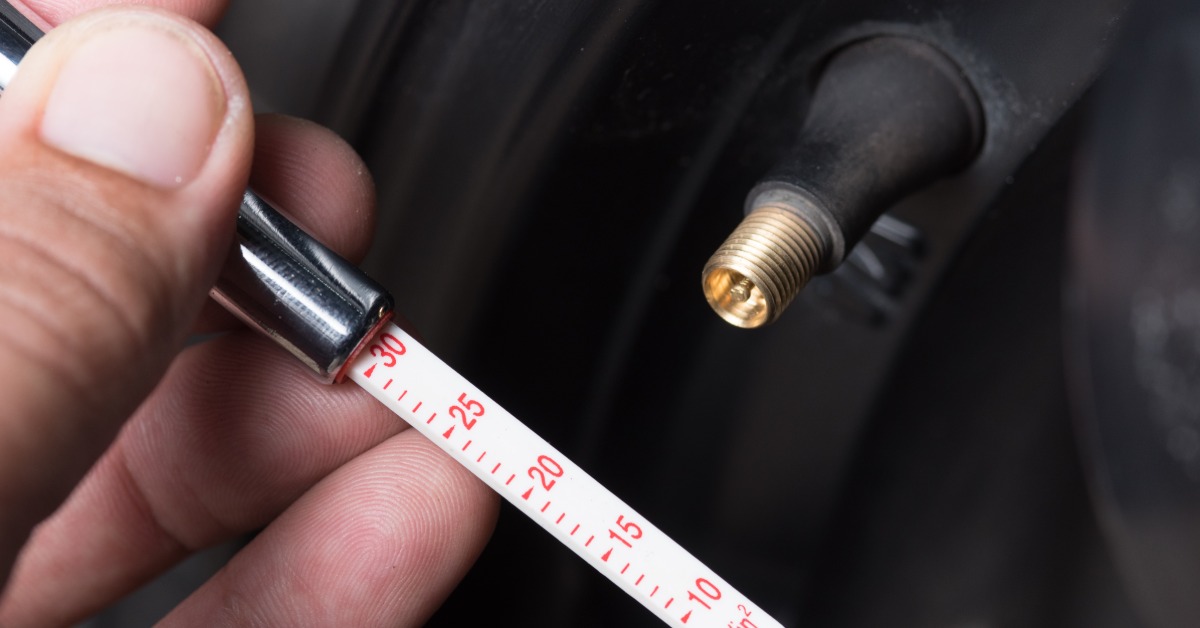 A close-up of a hand holding a tire pressure gauge next to the open brass tire valve stem of a tire.