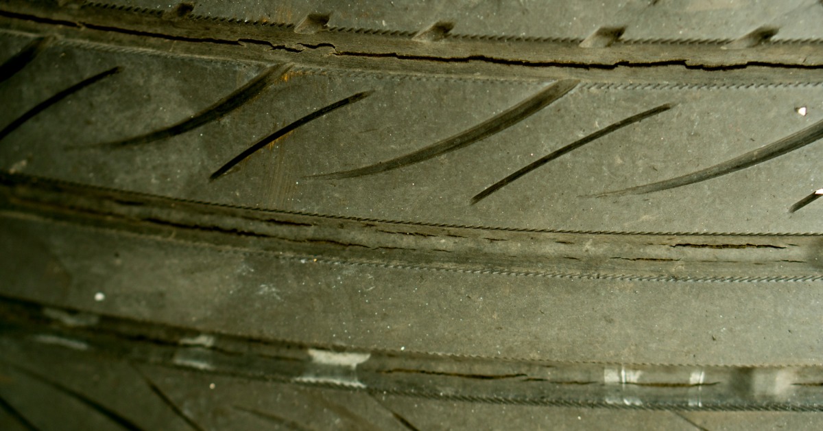 A close-up of the tread of an old and used tire with multiple long cracks from dry rot throughout the inner seams.