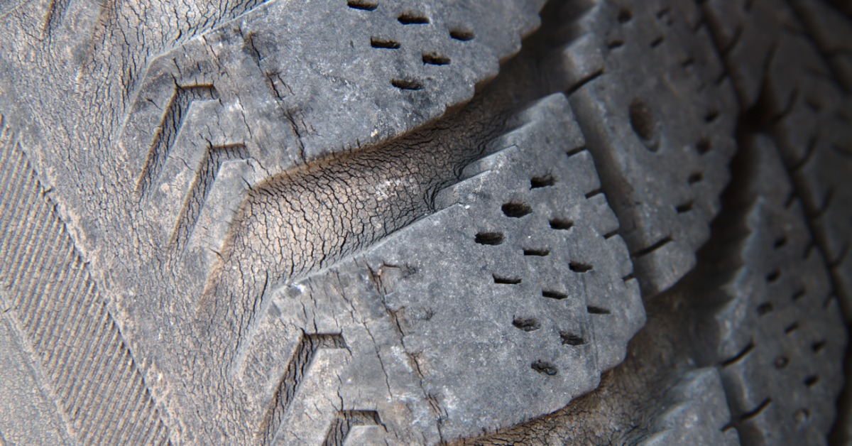 A close-up of the tire tread of an old, used tire with numerous cracks from dry rot along the tread.