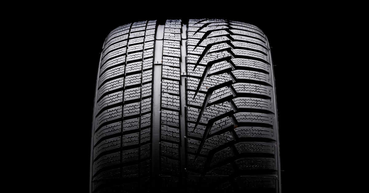 A close-up of a winter tire with an asymmetrical tire tread pattern upright against a black background.