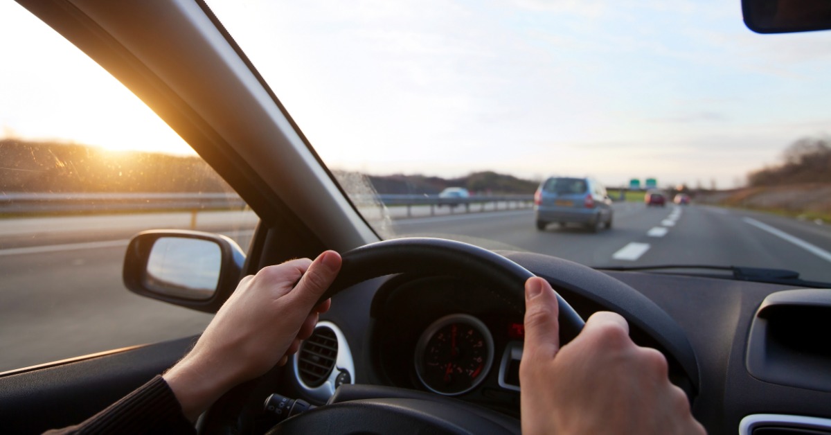 A person driving on the highway with other vehicles on the road. The person has two hands on the wheel.