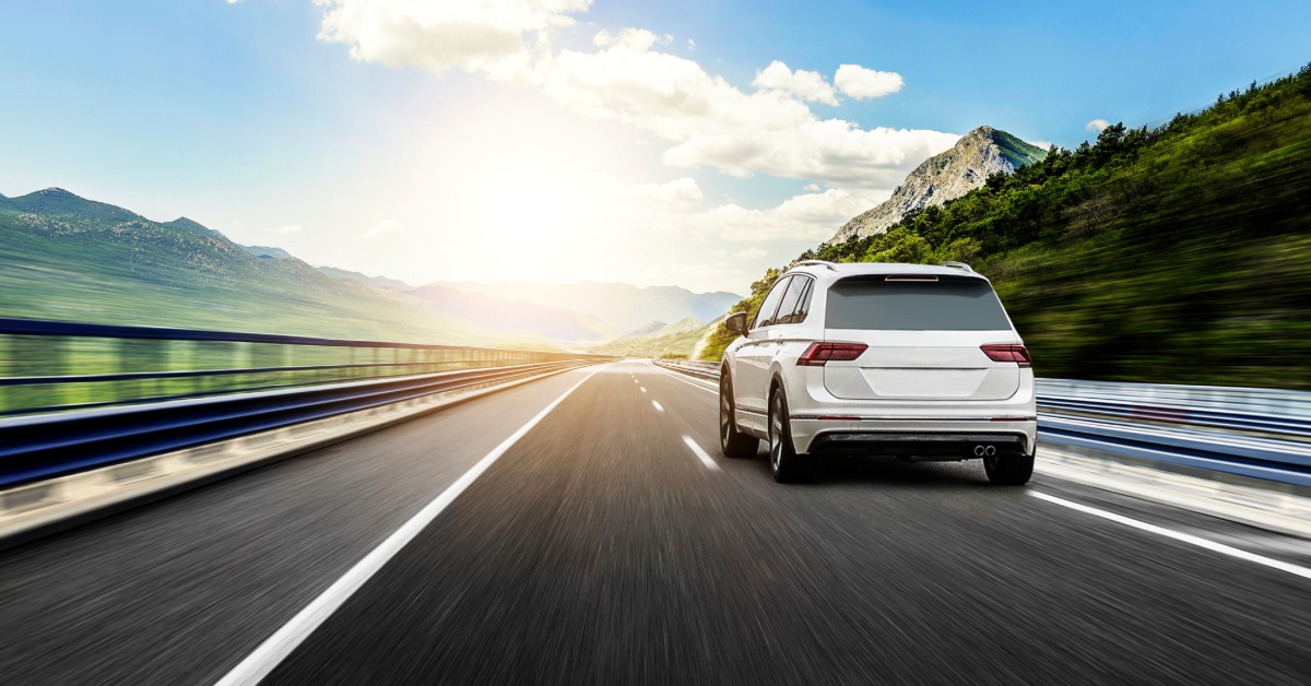 A car is rushing down a highway with mountains around the road. There are no other vehicles and the road is blurred.