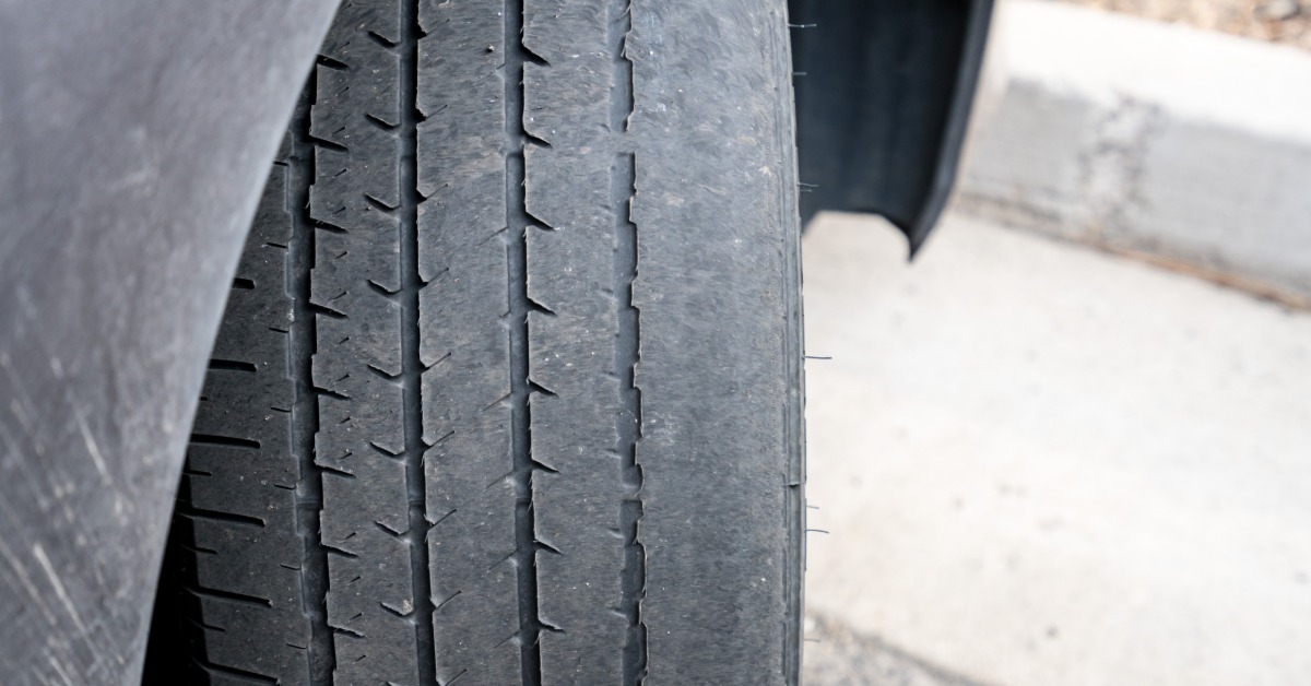 A tire connected to a car with the wheel turned outwards to show the tread. The tread is severely damaged and worn down.