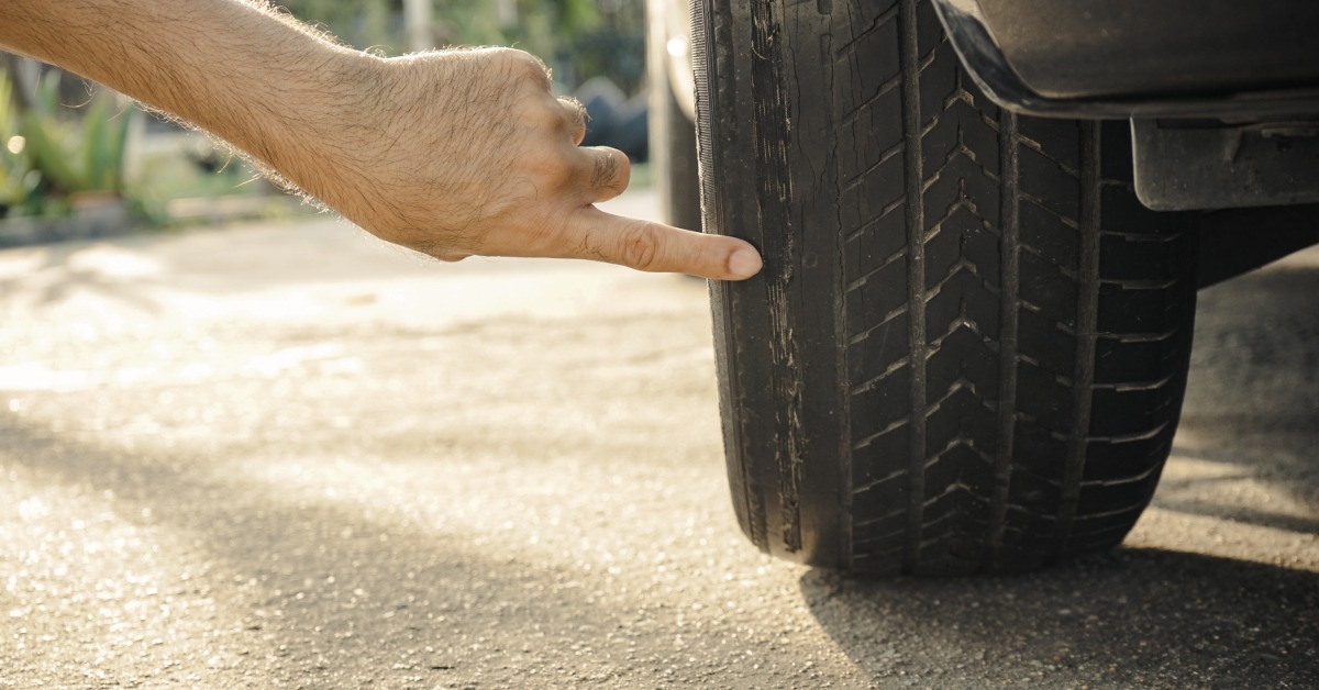 A man's hand pointing at the damage on a worn-out tire. The tread is worn down and balding in various spots.