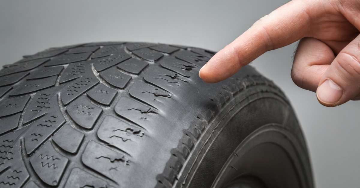 A person's hand pointing at minor damage to an older tire. The tread curves have small cuts on them.