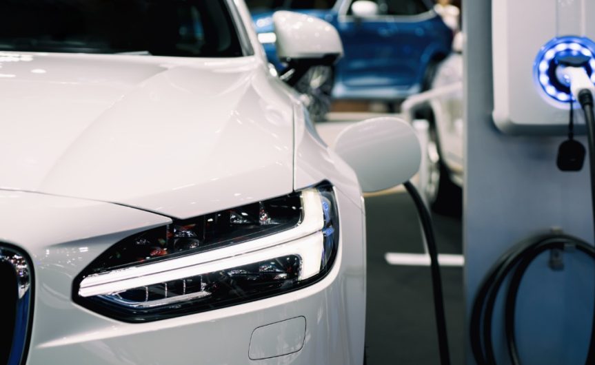 A white hybrid electric vehicle that is plugged into a charging battery. The vehicle is clean with no marks.