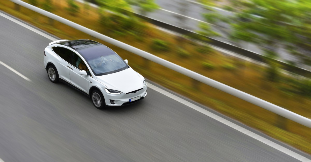 A modern electric vehicle driving on an empty highway. The car is moving fast, and the surroundings blur.