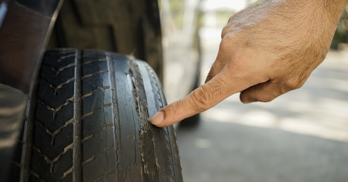 A person's hand pointing at the damage on an old tire. The tire has bald tread, making it unsafe to drive on.
