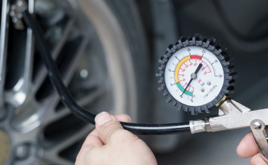 A close-up of someone using a tire pressure gauge to test the pressure in their vehicle's tire. The needle is in the green zone.