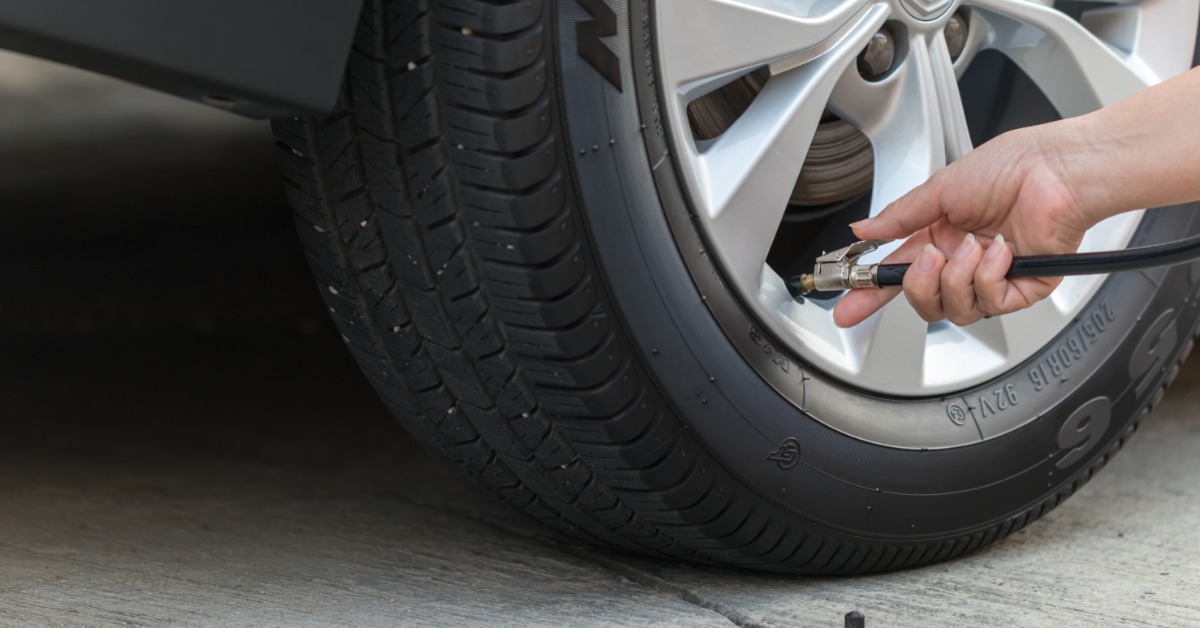 A close-up of someone holding a black air hose up to a tire valve. The tire looks clean and brand new.