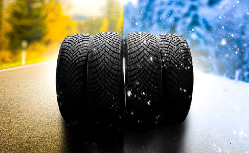 Four tires stacked next to each other on a road. The left side has changing tree colors, and the right side has snow falling.