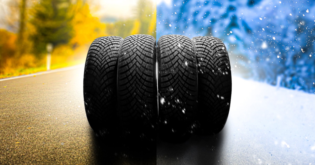 Four tires stacked next to each other on a road. The left side has changing tree colors, and the right side has snow falling.