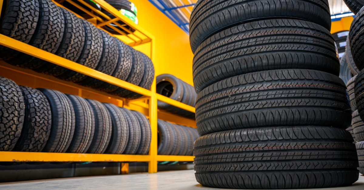 A stack of four tires on top of each other in a shop. Several other tires are on a shelf behind the stack.