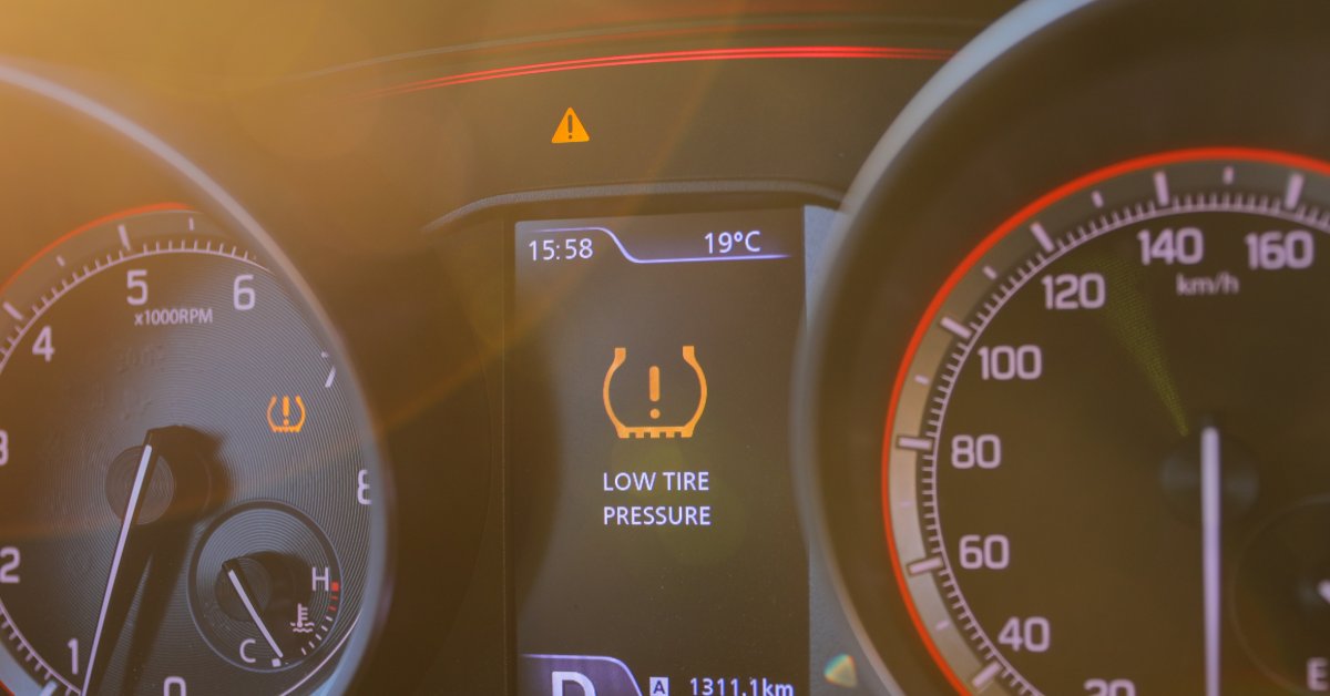 A close-up of the digital dashboard of a modern car with the "LOW TIRE PRESSURE" warning alert activated.