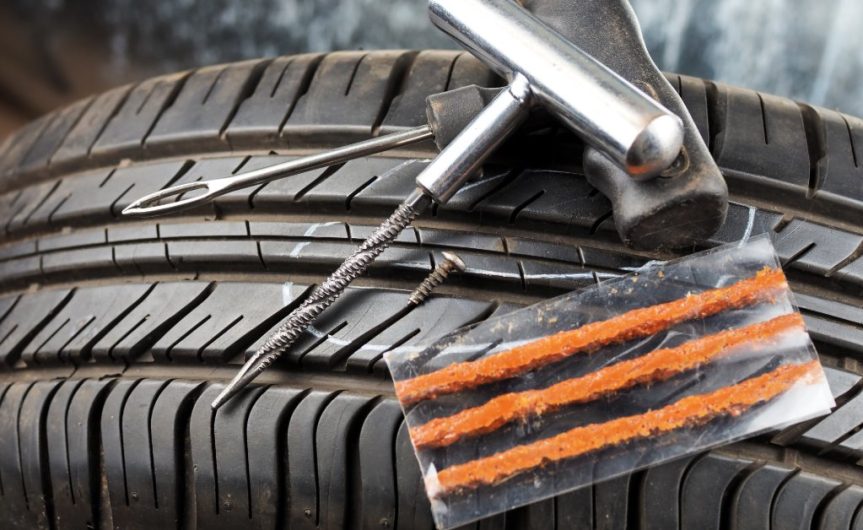 A close-up of a tire patch repair kit and its components resting on a car tire, including three orange patches.