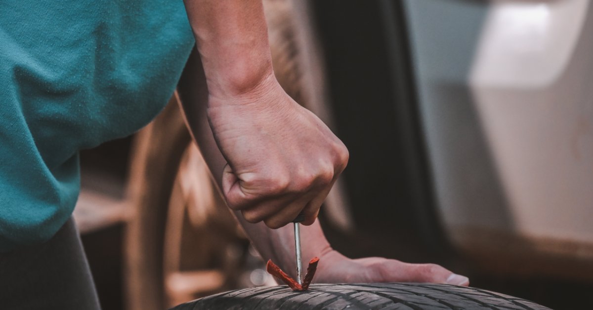 A close-up of a man's hand using the T-handle insertion tool to insert the orange vulcanized plug strings into a tire.