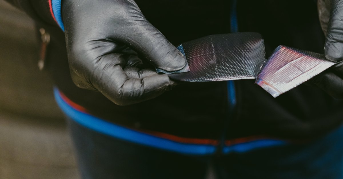 A close-up of a pair of hands with black rubber gloves removing the adhesive cover from a radial tire patch.