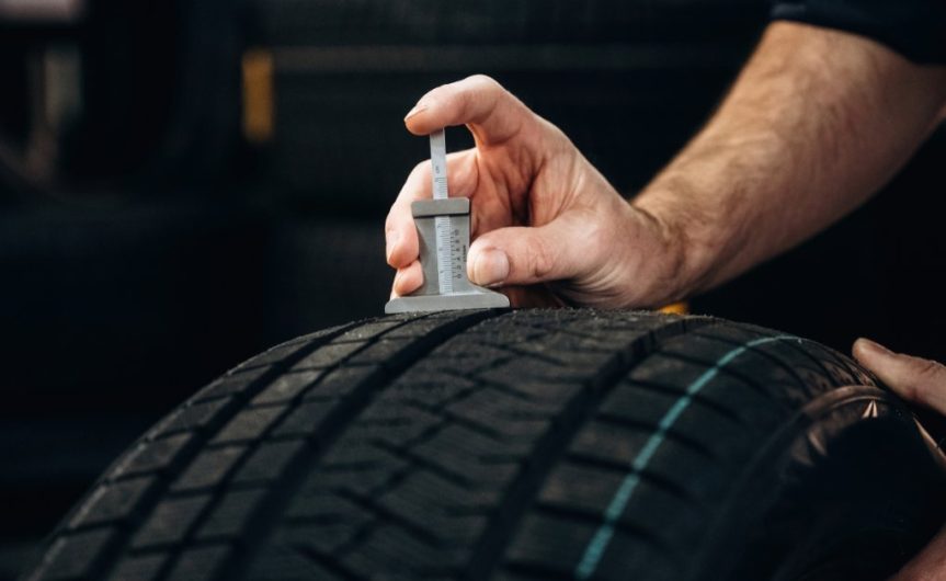 A close-up of someone inserting a tread depth gauge into one of the grooves of a tire to measure how worn the tread is.