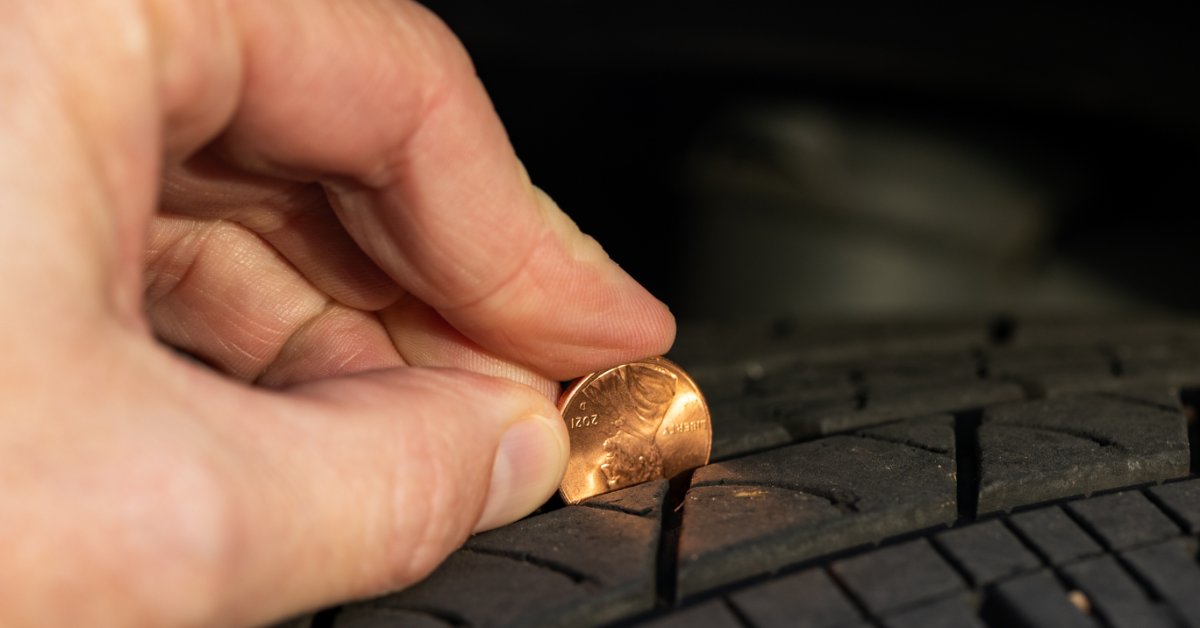 Someone inserts a penny with Lincoln's head facing down into the groove of a tire. Part of his head is covered.