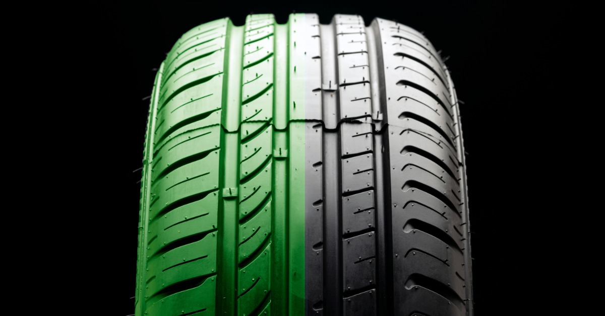 A close-up of a single upright car tire against a black background. Half of the tire is painted green.