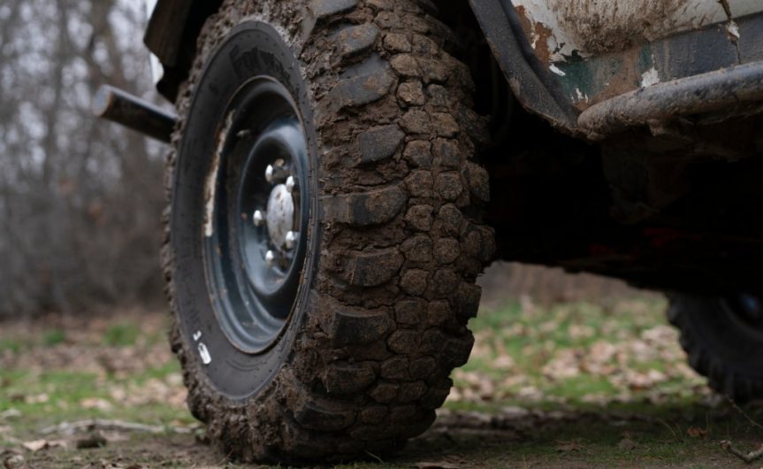 A close-up of a tire on a white truck. The tire has mud caked into the grooves, with mud splattered on the truck, too.