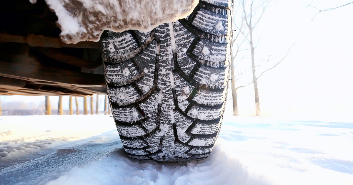 A close-up of the back of a tire parked on a thin layer of packed snow. Snow coats the tire's rubber.