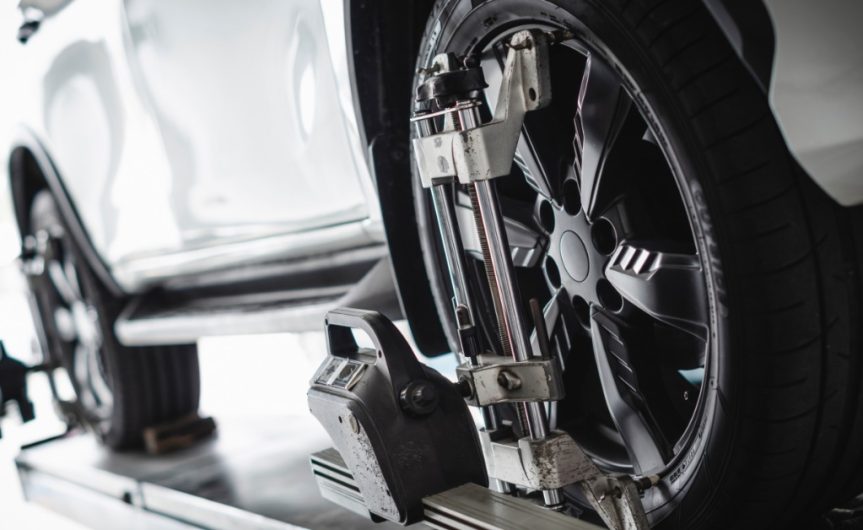 A SUV secured on a platform in an auto shop. Wheel alignment sensors are attached to the front and back wheels.