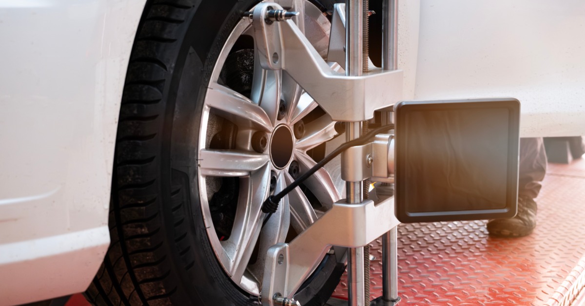 A close-up of a tire on a white car with a wheel alignment sensor attached to it. A red platform is next to the tire.