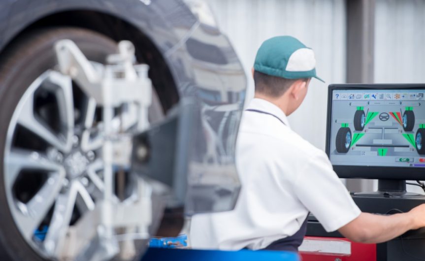 A long-distance, over-the-shoulder view of a man in a work shirt staring at a monitor with wheel and tire information.