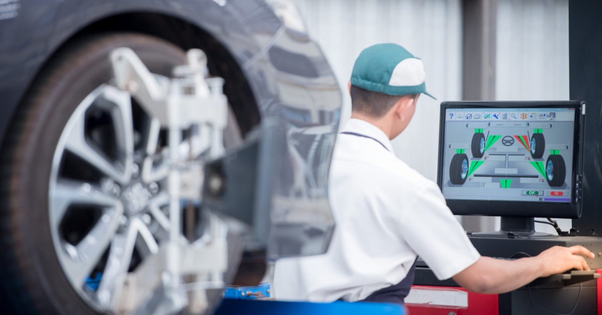 A long-distance, over-the-shoulder view of a man in a work shirt staring at a monitor with wheel and tire information.