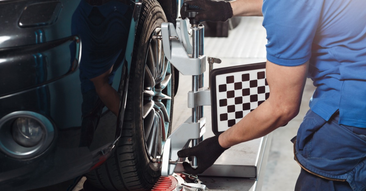 A close-up of a man in a blue shirt and black gloves using a grid sensor on the wheel of a car in an auto service shop.
