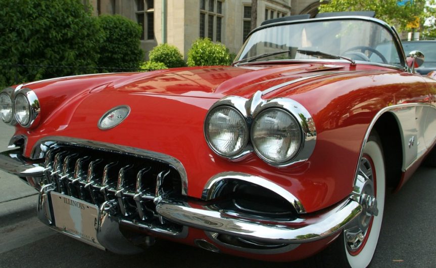 A close-up of the front of a classic red-and-white sports car with white-wall tires parked on a street.