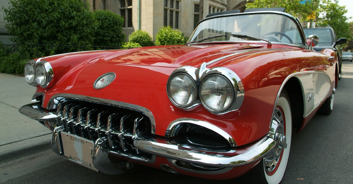 A close-up of the front of a classic red-and-white sports car with white-wall tires parked on a street.