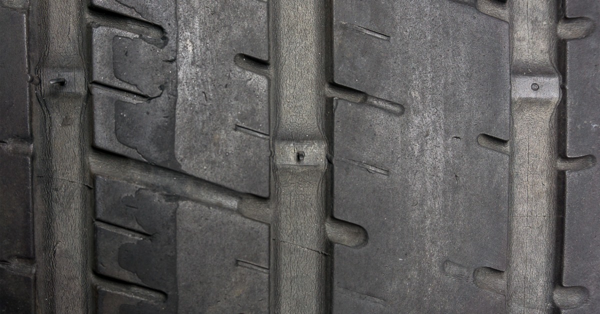 A close-up of a tire with worn tread. The tire and tread on the left side are more worn and shaved off.
