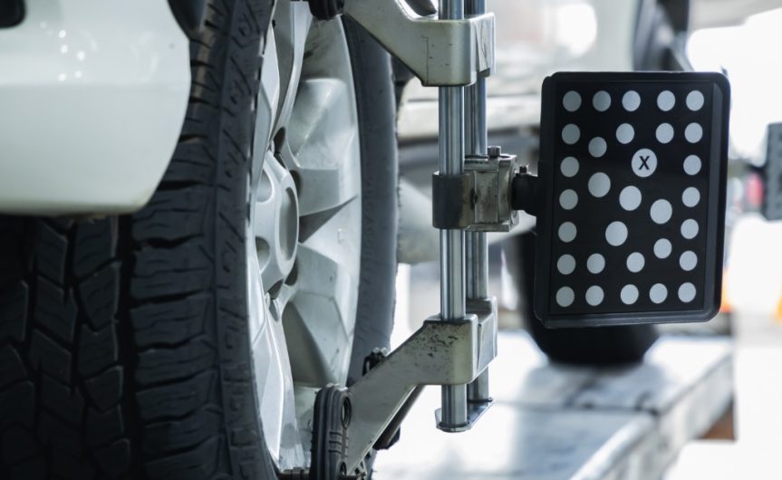 A close-up of a vehicle's tire with a wheel alignment target sensor clamped to the wheel. Another sensor is on the back tire, too.