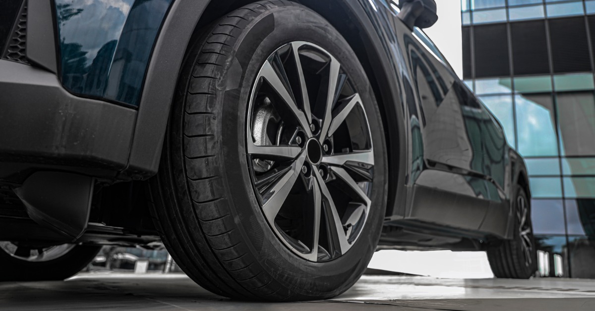 A close-up of a relatively new front tire on a black car parked in front of a building with lots of windows.