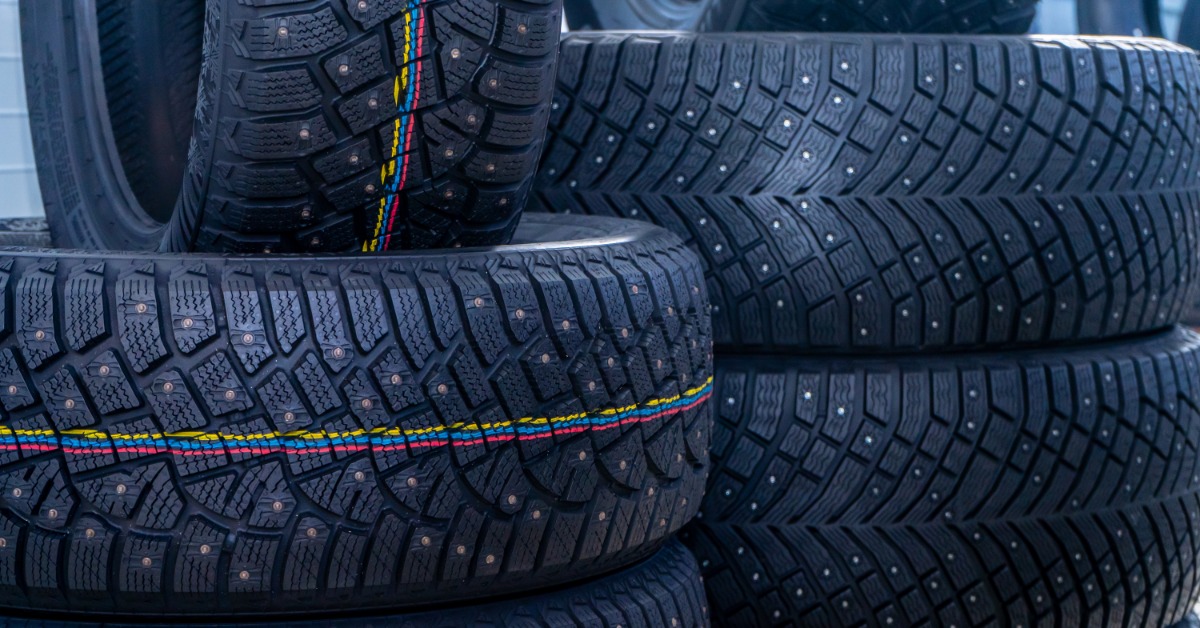 A stack of black car tires with visible studs and colorful tread lines arranged closely in overlapping rows.