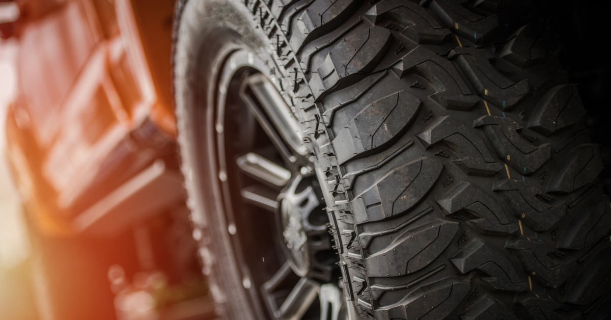 A close-up of the heavy-duty off-road tires and wheels of an orange pickup truck with a lift kit at sunset.