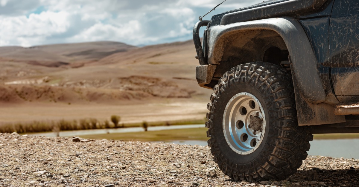 A close-up of the front off-road wheels and tires of a blue vehicle with a grille gate parked on a rocky ridge.